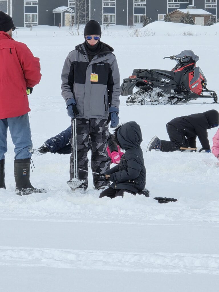 Lucas Roff, Program Manager at Inter-Tribal Council of Michigan assists an Ojibwe Charter School student with ice fishing at Waiska Bay behind Bay Mills Resort and Casino.